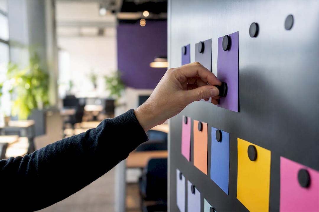 Hand arranging coloured task cards on a magnetic board in a modern office.